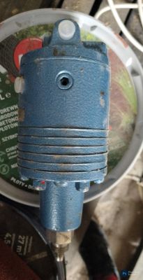 Niebieski metalowy element techniczny z wlotami na przewody ciśnieniowe, bez widocznej tabliczki znamionowej.