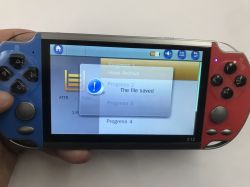 X12 handheld console in hands, blue-red body with “The file saved” popup on the screen