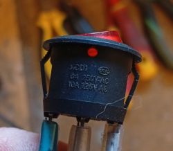 Tył podświetlanego przełącznika kołyskowego z trzema konektorami i oznaczeniami 250V AC