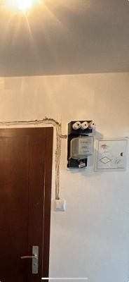 Zdjęcie ściany z zamontowanym licznikiem elektrycznym i bezpiecznikami obok drzwi.