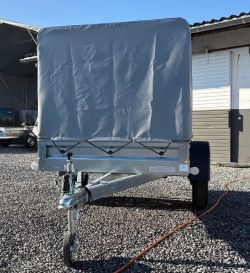 Front view of a trailer with a gray tarp on a gravel lot next to a building