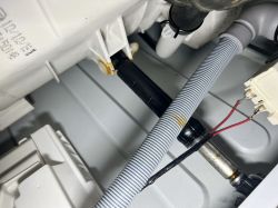 Widok wnętrza pralki Hotpoint z widocznym amortyzatorem i przewodami.