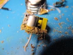 A damaged electronic module covered with brown corrosion or residue on a blue surface.