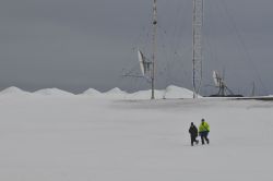 Walking in a Snowy Landscape with Satellite Dishes Two people walking in a snowy landscape with satellite dishes in the background.