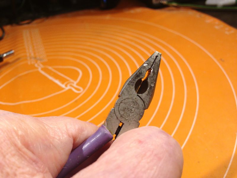 Stare, zużyte kombinerki trzymane w dłoni na pomarańczowym tle.