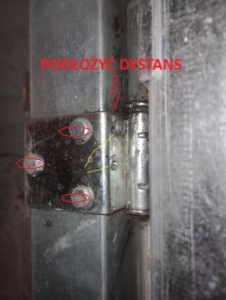 Zbliżenie na metalowy zawias z zaznaczonymi śrubami i napisem „POŁOŻYĆ DYSTANS”