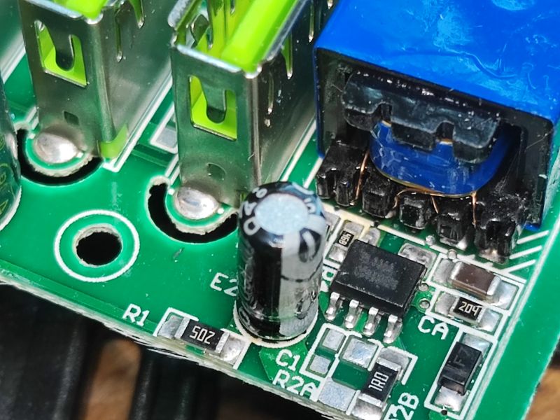 Zbliżenie na płytkę drukowaną z portami USB, kondensatorem i transformatorem.