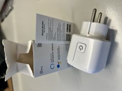 White smart plug with power button and user manual next to opened packaging