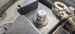 Zbliżenie na biegun akumulatora samochodowego i metalową klemę obok w komorze silnika.