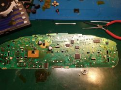 Płytka drukowana z elementami elektronicznymi na zielonym stole warsztatowym.