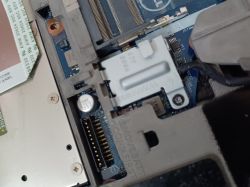 Zbliżenie na wnętrze laptopa z ukrytą płytą główną i zapieczoną śrubką obok złącza.