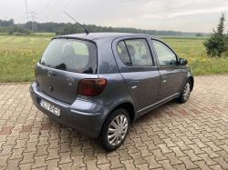 Gray Toyota Yaris GA car parked on a paved area with fields in the background.