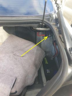Car trunk interior with yellow arrow pointing to a red power cable connection