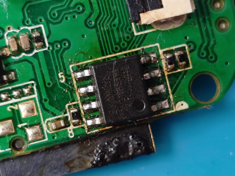 Close-up of a green printed circuit board with a visible black integrated circuit and copper traces.