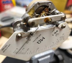 Zbliżenie wnętrza miernika IMI-1 z mechanizmem i tarczą skali MΩ w warsztatowym tle.