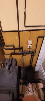 Widok starego pieca i instalacji grzewczej z okablowaniem na ścianie.