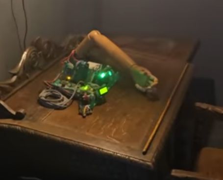 Elektroniczny układ z podświetlonymi diodami LED i mechanicznym ramieniem na drewnianym stole.