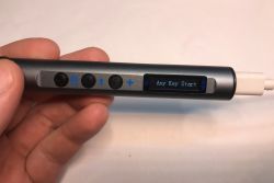 A hand holding an electronic soldering iron with an OLED display, three buttons, and a USB-C connector.