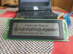 LCD module showing “Internet Radio” and “Connecting to network” on a table, with a laptop in the background.