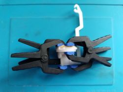 Compressing Valve Membrane with LUX-TOOLS Clamps and Coin Two LUX-TOOLS spring clamps compressing a valve membrane to a plastic control chamber element, with a 1 zł coin placed between the clamp jaw and the membrane; clear silicone adhesive visible on marked sections.