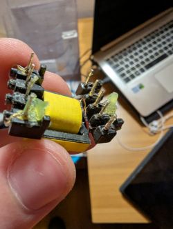 Electronic transformer held between fingers in front of a laptop on a desk.