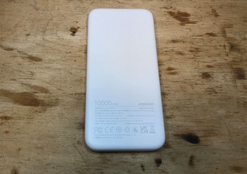 Powerbank JR-QP194 na drewnianym stole z widocznymi oznaczeniami technicznymi i pojemnością 10000 mAh.
