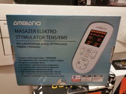 Opakowanie masażera elektrostymulatora TENS/EMS marki Ambiano na tle innych urządzeń elektronicznych.