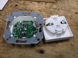 Interior of disassembled SWP86-01OG smart socket Disassembled smart electrical socket with exposed PCB and mechanical part on a wooden surface.