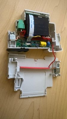 Disassembled device housing with PCB, transformer, wires, and connector on a wooden surface