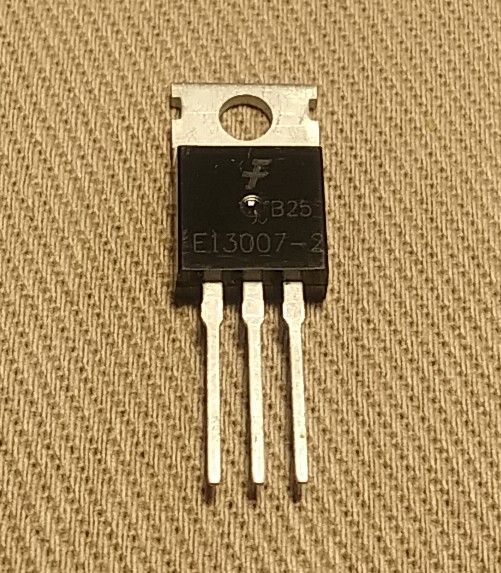 Transistor in a TO-220 package with three legs, on a fabric background.