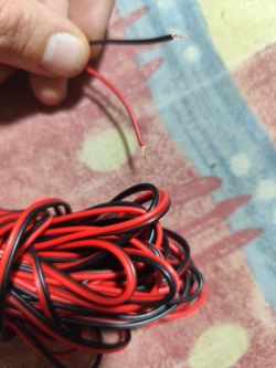 Czerwono-czarny kabel z odsłoniętymi końcówkami trzymany w rękach.