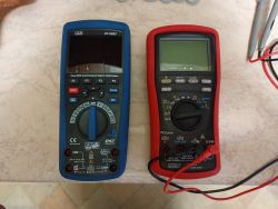 Dwa multimetry cyfrowe na blacie: niebieski CEM DT-9987 i czerwony Brymen z przewodami