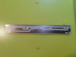 Narrow double-sided PCB with white traces and mounting holes on a copper surface