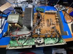 Rozłożone urządzenie audio z widoczną płytą PCB, transformatorem, radiatorem i okablowaniem na stole warsztatowym