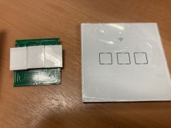 Two components of a device: a circuit board with three buttons and a touch panel with three fields on a wooden surface.