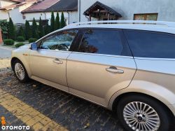 A beige Ford station wagon parked next to a house on paving stones.