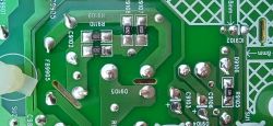 Fragment zielonej płytki drukowanej PCB z widocznymi oznaczeniami elementów, ścieżkami i lutowanymi komponentami.