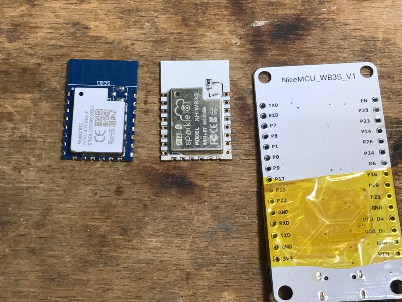 NiceMCU and CB3S Modules on Wooden Table Three different electronic modules lying on a wooden table, including NiceMCU_WB3S_V1 with visible pin labels.