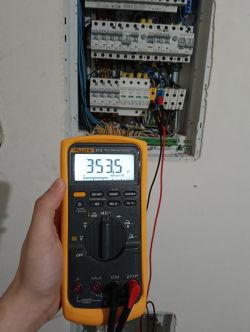 Ręka trzymająca miernik Fluke przed rozdzielnicą elektryczną.