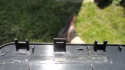 Zbliżenie na uszkodzone zaczepy plastikowej obudowy powerbanku na tle trawy.