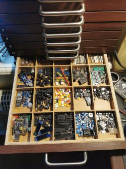 Szuflada z drewnianymi przegródkami wypełniona elementami elektronicznymi.