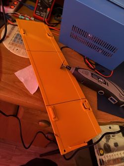 Yellow plastic panel on a workbench beside a rotary tool and a blue vented device housing