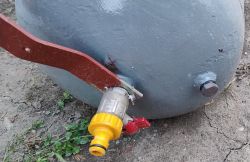Fragment metalowego walca, wykonanego ze starej butli LPG, z przyspawanym zaworem ogrodowym i uchwytem.