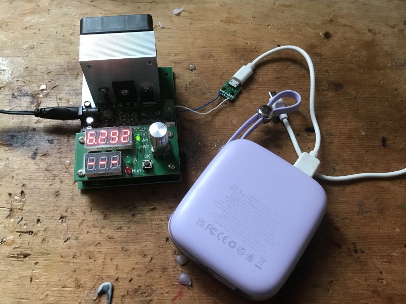 Powerbank JR-L002 w trakcie testu pojemności na drewnianym stole obok miernika.