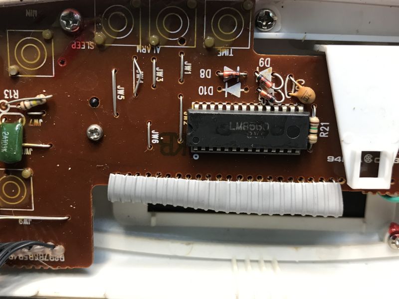 Close-up of a brown PCB with an LM8560 IC and a ribbon connector inside a device housing