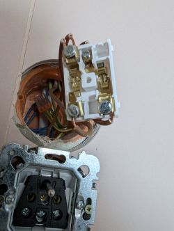 Podwójny włącznik elektryczny z odkrytymi przewodami w puszce ściennej.