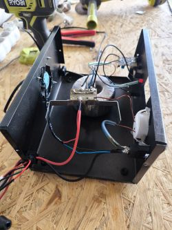 Interior of an open battery charger with visible wiring and transformers on a workbench.