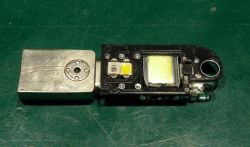 Otwarta miniaturowa elektronika z diodami LED i akumulatorem obok metalowej obudowy na zielonym tle