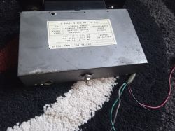 Metalowa skrzynka elektroniczna z etykietą i wystającymi przewodami na dywanie.