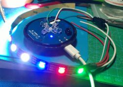 Close-up of an electronic module with a WS2812 LED strip connected to a connector, with LEDs shining in different colors.